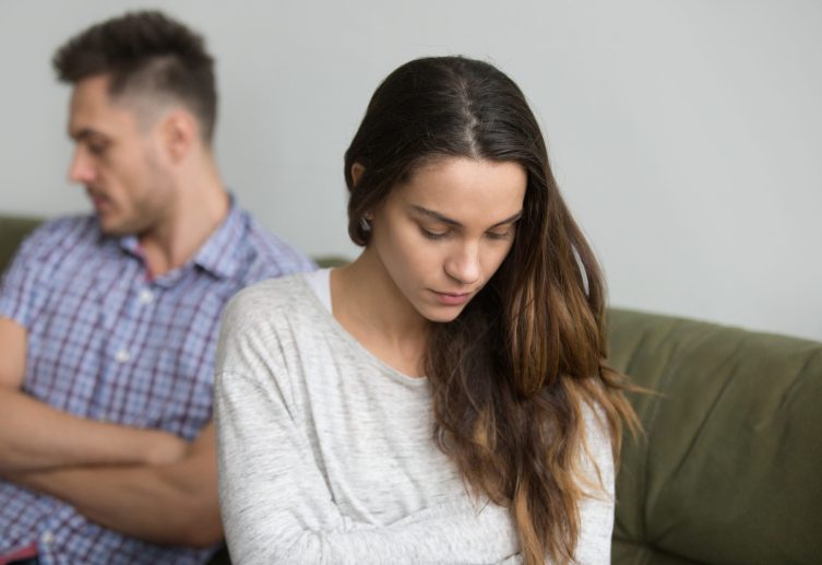 Concerned serious wife sad about family problem, thinking about relationships ending, husband sitting behind being ignorant and indifferent. Concept of spouse break up, unsuccessful marriage, quarrel